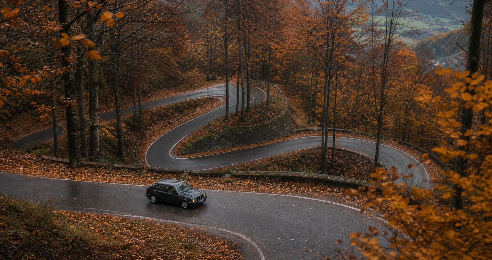 A car on autumn hairpins in a forested valley.